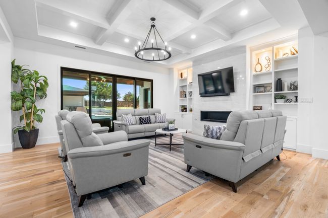 Living area featuring a chandelier, light wood-style floors, baseboards, coffered ceiling, and a fireplace | Image 6