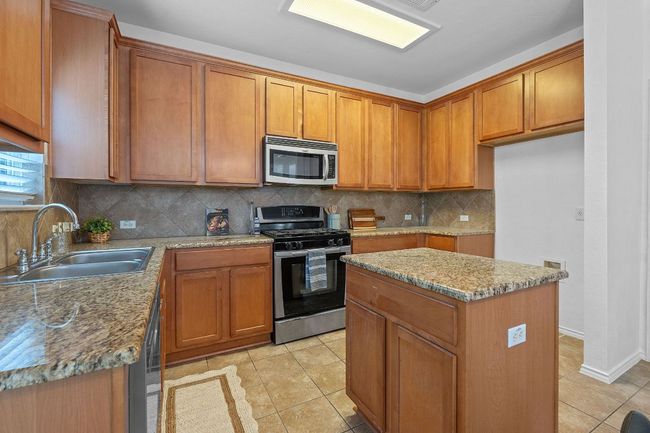Kitchen featuring stainless steel appliances, a sink, brown cabinets, light tile patterned flooring, and tasteful backsplash | Image 11