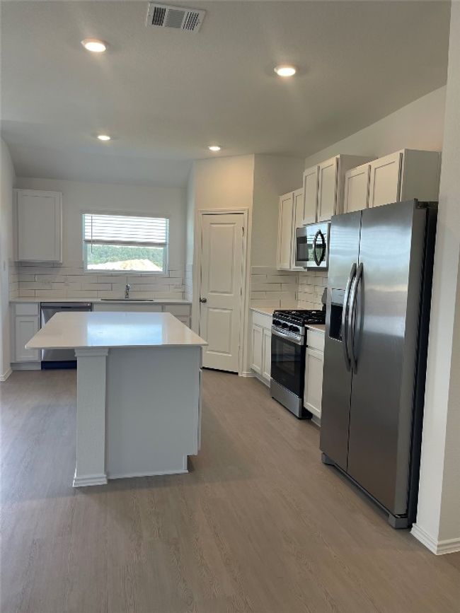 Kitchen featuring appliances with stainless steel finishes, light countertops, backsplash, light wood-type flooring, and a center island | Image 7