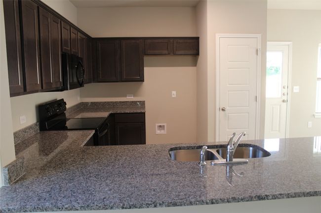 Kitchen featuring black appliances, dark brown cabinets, dark stone countertops, and a sink | Image 5