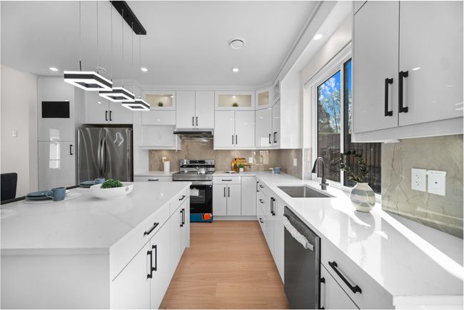 Kitchen with appliances with stainless steel finishes, under cabinet range hood, white cabinets, decorative light fixtures, and glass insert cabinets | Image 7