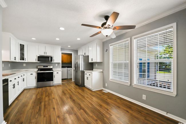 Kitchen featuring stainless steel appliances, washing machine and dryer, white cabinets, a ceiling fan, and baseboards | Image 9