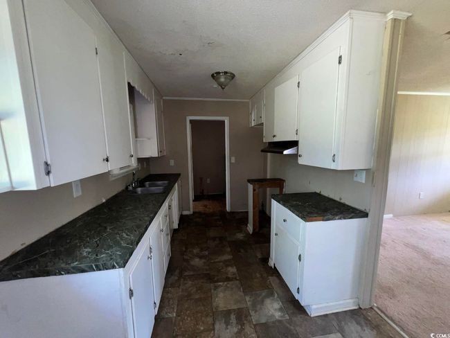 Kitchen with under cabinet range hood, a sink, white cabinetry, and dark countertops | Image 4