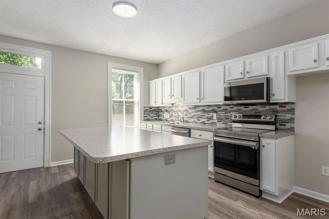 Kitchen with stainless steel appliances, backsplash, dark wood-type flooring, a kitchen island, and light countertops | Image 7