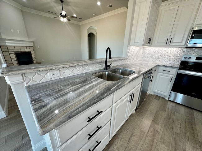 Kitchen featuring stainless steel appliances, a sink, wood finished floors, stone counters, and ornamental molding | Image 8