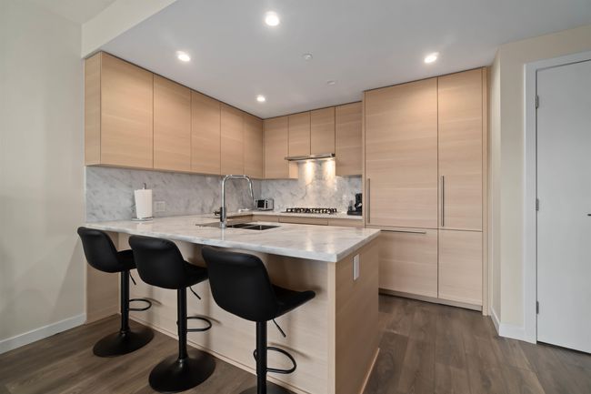 Kitchen featuring dark wood finished floors, light brown cabinets, a kitchen bar, and a sink | Image 15