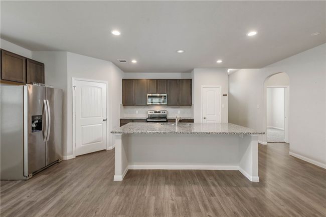 Kitchen with appliances with stainless steel finishes, arched walkways, wood finished floors, dark brown cabinets, and recessed lighting | Image 4