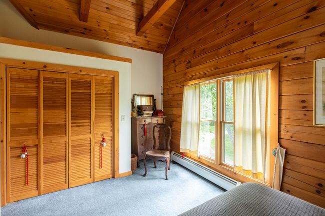 Bedroom featuring carpet flooring, wooden walls, a baseboard radiator, wooden ceiling, and a closet | Image 17