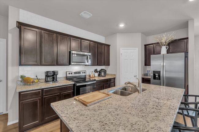 Kitchen with stainless steel appliances, a sink, dark brown cabinets, a kitchen breakfast bar, and an island with sink | Image 19