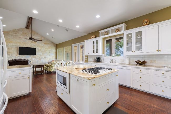 Kitchen featuring a kitchen island, backsplash, a sink, open floor plan, and white appliances | Image 6