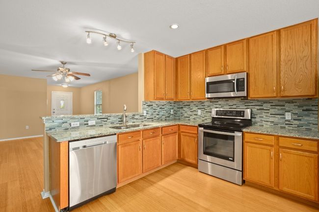 Kitchen with stainless steel appliances, a sink, light wood-type flooring, decorative backsplash, and a ceiling fan | Image 8