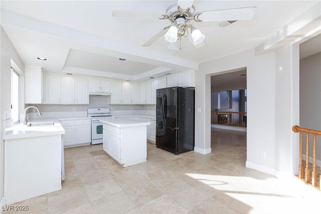 Kitchen with ceiling fan, freestanding refrigerator, white gas stove, light countertops, and a sink | Image 13