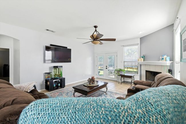 Living area with ceiling fan, arched walkways, tile patterned flooring, a tiled fireplace, and french doors | Image 6