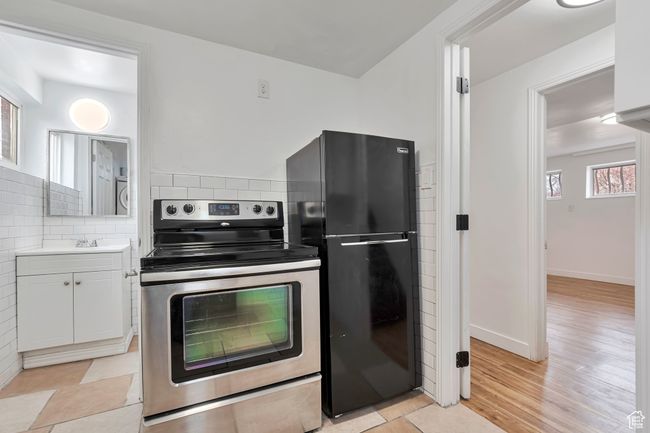Kitchen with electric range, freestanding refrigerator, light countertops, white cabinetry, and backsplash | Image 14