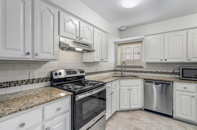 Kitchen featuring a sink, stainless steel appliances, white cabinetry, and under cabinet range hood | Image 10