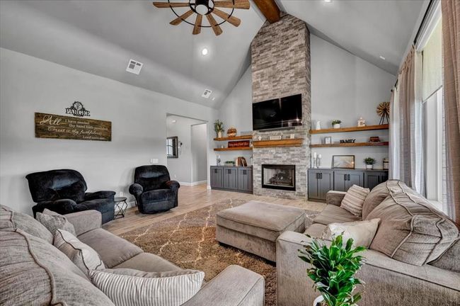 Living area with a ceiling fan, high vaulted ceiling, light wood-type flooring, beam ceiling, and a stone fireplace | Image 16