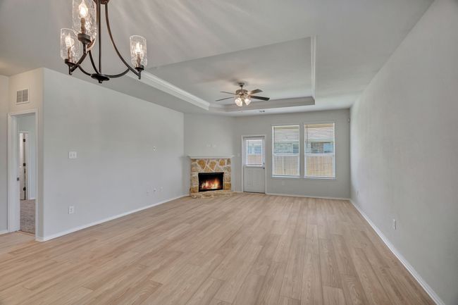 Unfurnished living room with a tray ceiling, light wood-style flooring, a chandelier, a ceiling fan, and a stone fireplace | Image 14