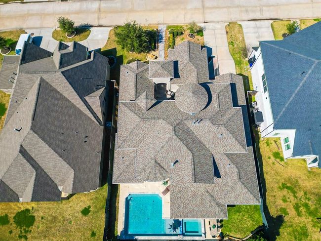 This aerial view showcases a spacious home with an intricate roof design, a private backyard, and a swimming pool. The property is part of a well-maintained neighborhood with nearby green spaces and a wide street for easy access. | Image 48