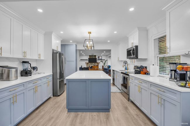 Kitchen with stainless steel appliances, a center island, light wood-style flooring, crown molding, and white cabinets | Image 9