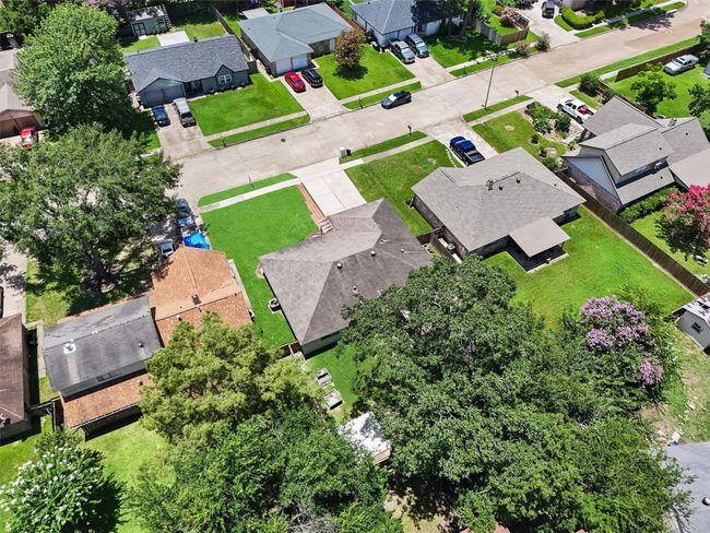 This aerial view showcases a suburban neighborhood with well-maintained homes and lush green lawns. The houses have spacious yards and are surrounded by mature trees, offering a serene and inviting atmosphere. The streets are clean and lined with neatly parked cars, indicating a quiet and orderly community. | Image 28