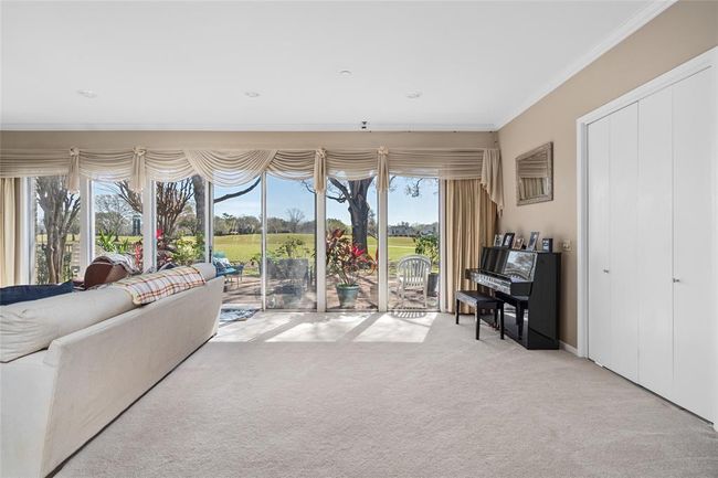 This bright and inviting living area showcases floor-to-ceiling windows that offer stunning views of the golf course and fill the space with natural light. Plush carpeting adds warmth, while the neutral-toned walls create a relaxing ambiance. Sliding glass doors lead to the outdoor patio, seamlessly blending indoor and outdoor living. | Image 14
