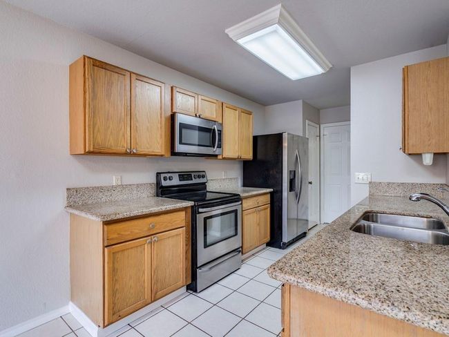 Kitchen with appliances with stainless steel finishes, light tile patterned flooring, and light stone countertops | Image 13