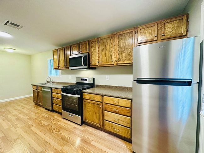 Kitchen with appliances with stainless steel finishes, light wood-type flooring, brown cabinetry, and dark countertops | Image 4