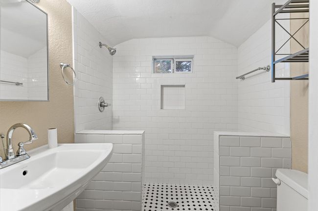 Bathroom featuring a sink, walk in shower, toilet, a textured wall, and vaulted ceiling | Image 30