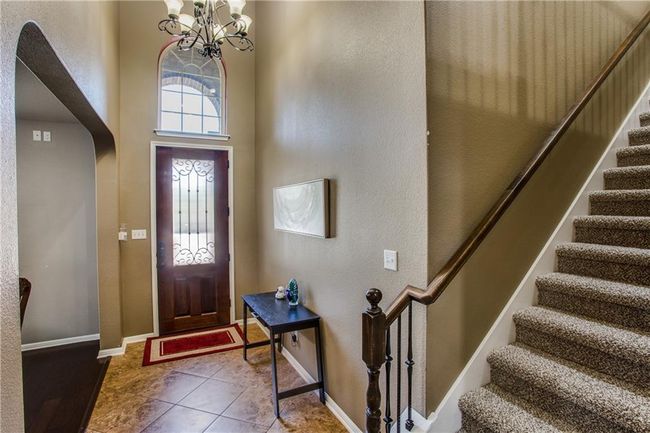 Tiled foyer entrance with stairs, arched walkways, a chandelier, a towering ceiling, and a textured wall | Image 5