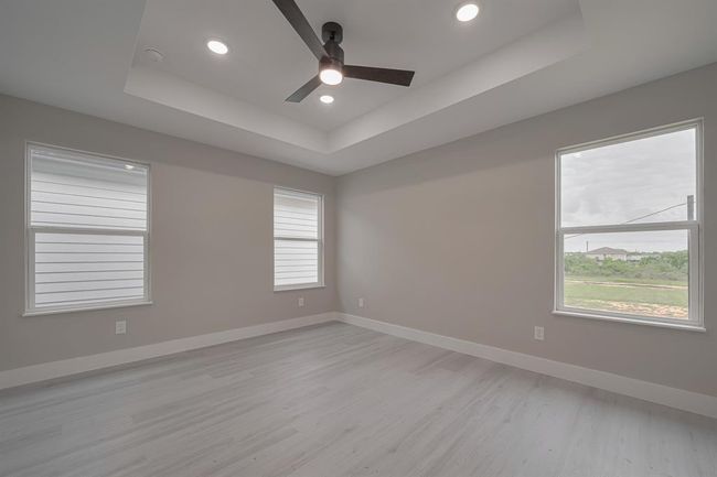 Airy and expansive, the primary bedroom showcases multiple large windows, a tray ceiling with recessed lighting, and a modern ceiling fan for added comfort. | Image 20