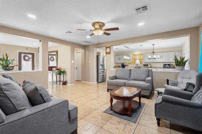 Living area with ceiling fan with notable chandelier, visible vents, and light tile patterned floors | Image 10