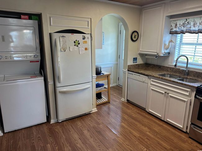 Kitchen with white appliances, stacked washing machine and dryer, arched walkways, and dark wood finished floors | Image 8