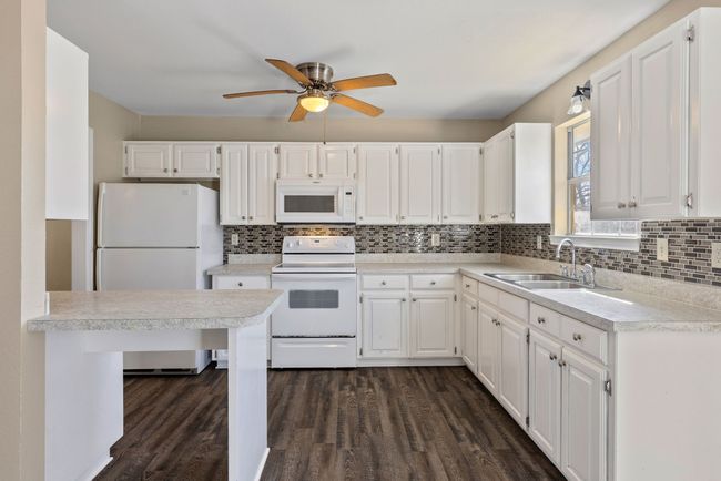Kitchen featuring white appliances, white cabinets, dark wood-type flooring, light countertops, and a sink | Image 14