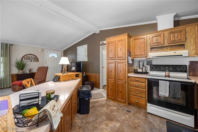 Kitchen with electric range oven, exhaust hood, light countertops, crown molding, and wooden walls | Image 25