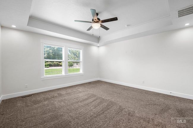 Empty room with a raised ceiling, ornamental molding, ceiling fan, carpet floors, and recessed lighting | Image 16
