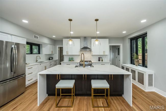 Kitchen with freestanding refrigerator, wall chimney exhaust hood, backsplash, a kitchen bar, and light wood-type flooring | Image 10
