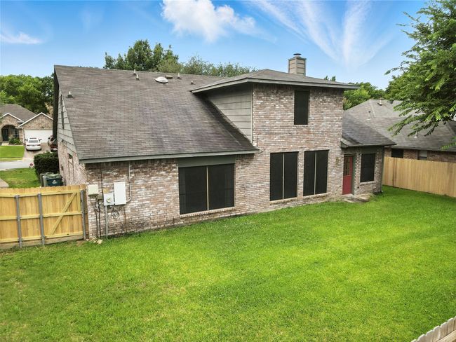 Back of house featuring a chimney, a fenced backyard, brick siding, and a shingled roof | Image 36