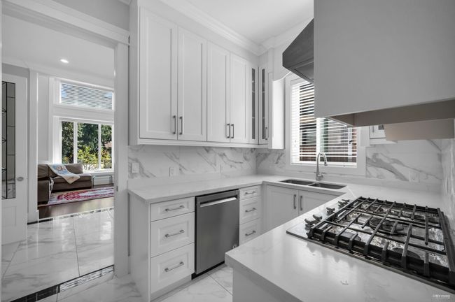 Kitchen featuring appliances with stainless steel finishes, light marble finish flooring, white cabinets, light stone counters, and ornamental molding | Image 13