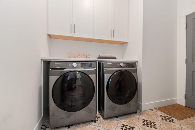 Clothes washing area featuring light tile patterned flooring, cabinet space, independent washer and dryer, and baseboards | Image 24