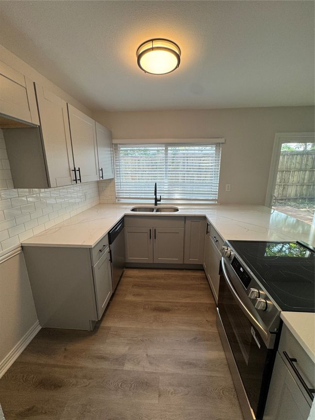 Kitchen featuring range, a sink, dishwashing machine, gray cabinetry, and light stone countertops | Image 4