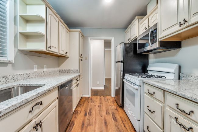Kitchen with appliances, shelves, light wood-look flooring, and light stone counters | Image 11