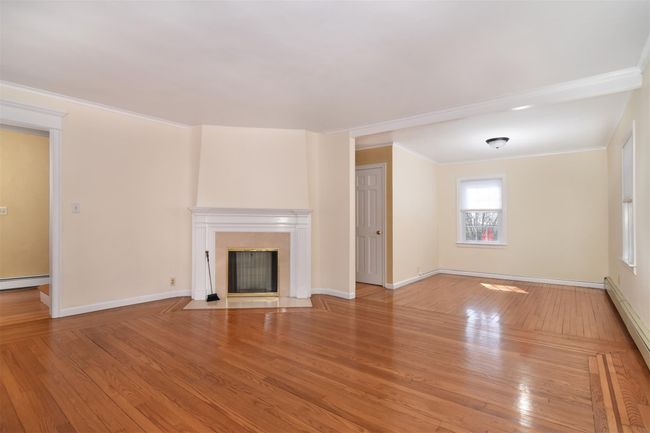 Unfurnished living room with dining room view featuring ornamental molding, a baseboard heating unit, baseboards, and wood finished floors | Image 4