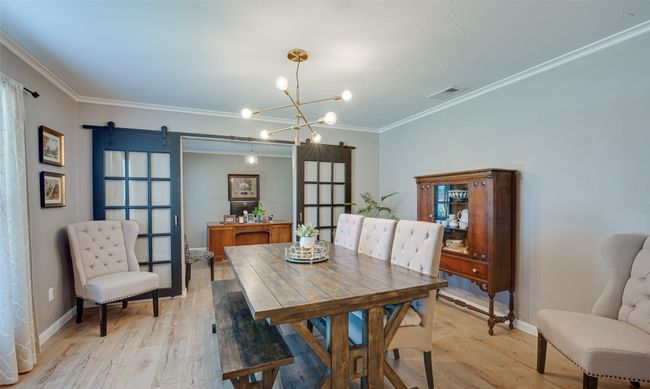 Dining space featuring a barn door, light wood-type flooring, ornamental molding, and a chandelier | Image 5
