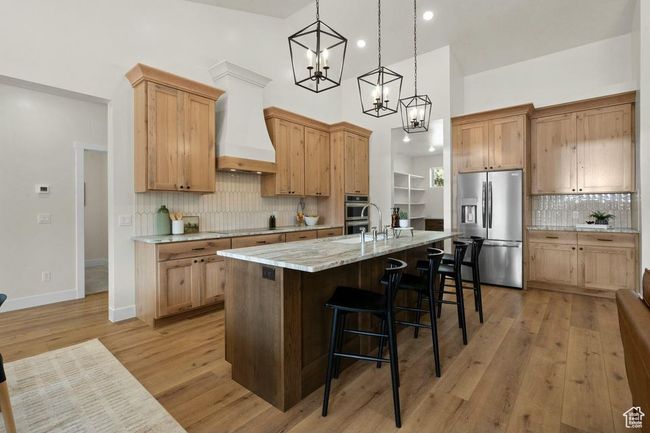 Kitchen with an island with sink, premium range hood, light wood-style floors, appliances with stainless steel finishes, and a breakfast bar area | Image 8