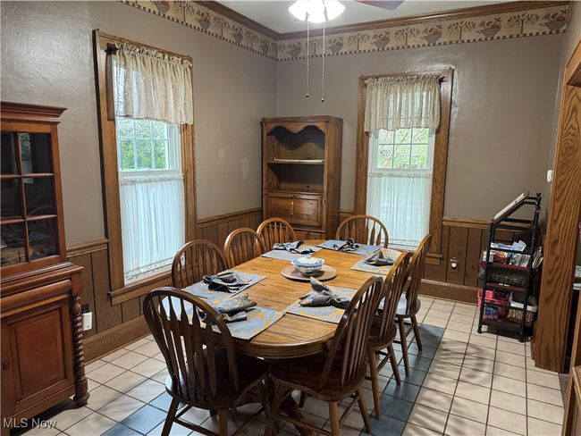 Dining space featuring light tile patterned floors, a healthy amount of sunlight, a ceiling fan, and wainscoting | Image 7