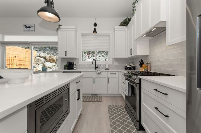 Kitchen featuring stainless steel appliances, white cabinets, tasteful backsplash, light countertops, and a sink | Image 13