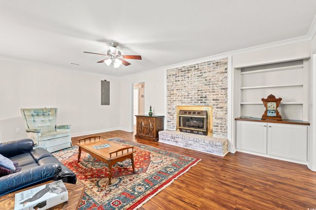 Living room featuring wood finished floors, electric panel, ornamental molding, a ceiling fan, and a fireplace | Image 8
