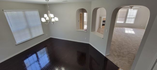 Unfurnished dining area with a ceiling fan, arched walkways, a chandelier, and dark colored carpet | Image 6