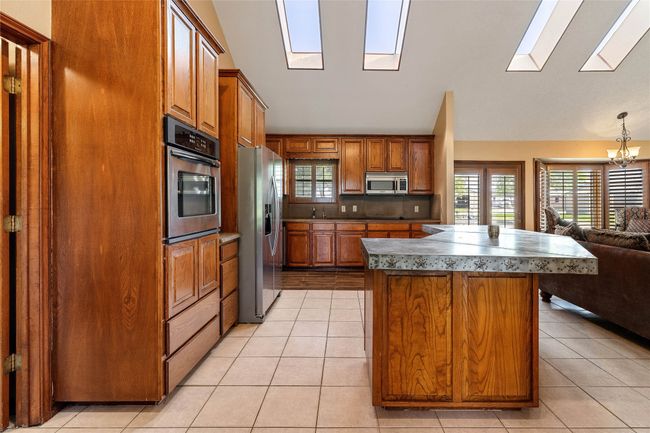 Kitchen featuring stainless steel appliances, a skylight, a chandelier, brown cabinets, and open floor plan | Image 9