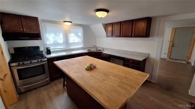 Kitchen with a sink, under cabinet range hood, dark brown cabinets, wood finished floors, and stainless steel appliances | Image 17